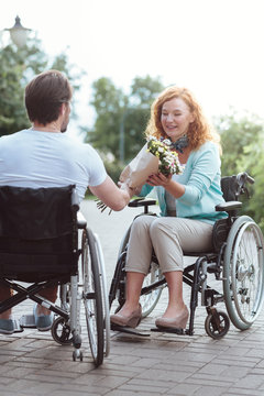 This is for you. Selective focus on a beautiful woman sitting in a wheelchair smiling while receiving flowers from her soulmate.