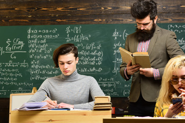 Attentive students writing something in their note pads while sitting at desks in the classroom. Students are communicating on regular basis with the tutor.