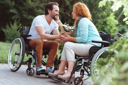 Forever together. Loving husband and wife sitting on their wheelchairs and smiling cheerfully while talking sweet words and enjoying pleasant conversation.