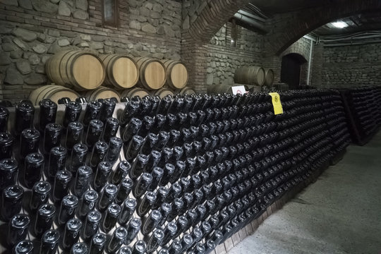 Ancient wine cellar with oak barrels and shelves with bottles of red wine and champagne