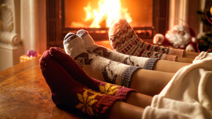 Young family wearing warm woolen socks and lying under blanket relaxing at fireplace