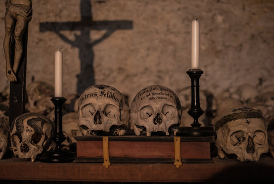 Decorated skulls in the Parish Church of Hallstatt. Vintage candlesticks and crucifix casting shadows on the wall of the crypt
