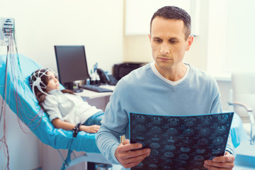 I am so scared. Waist up shot of a stressed father analyzing a computed tomography scan while his little daughter undergoing electroencephalography procedure.