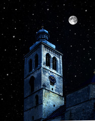 Tower of the Gothic church against a background of night sky with stars and full moon