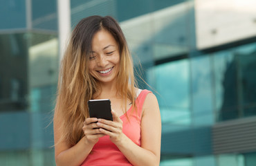 Happy young Asian woman with smartphone standing in the street