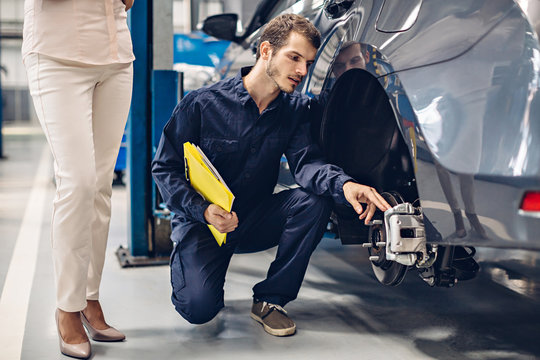 Auto Car Repair Service Center. A Female Customer And Mechanic Checking Car Breaks