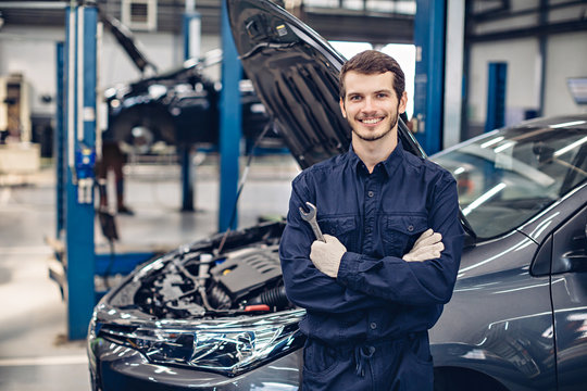 Auto car repair service center. Happy mechanic standing by the car