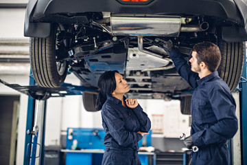 Auto car repair service center. Two mechanics - man and woman examining car