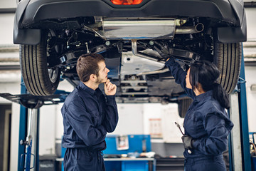 Auto car repair service center. Two mechanics - man and woman examining car