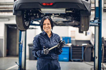 Auto car repair service center. Happy female mechanic standing by the car - Powered by Adobe