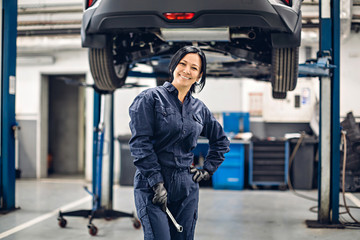 Auto car repair service center. Happy female mechanic standing by the car
