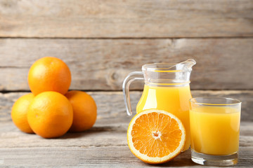 Fototapeta na wymiar Orange fruit with jug and glass of juice on grey wooden table
