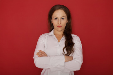 Charming businesswoman. Confident young businesswoman keeping arms crossed and looking at camera while standing against red background