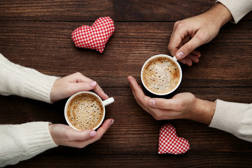 Female and male hand holding cups of coffee with red fabric hearts