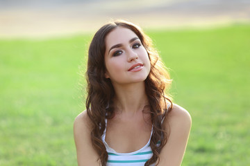 Fototapeta premium Portrait of young woman sitting on green grass in the park