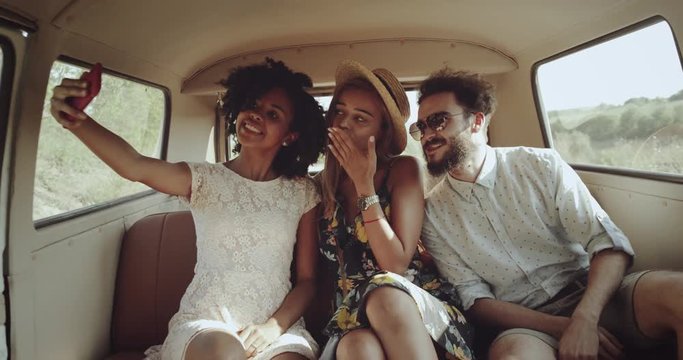 Selfie time in a retro vintage bus , two charismatics girls and one man taking pictures using a phone , they wearing boho style clothes.