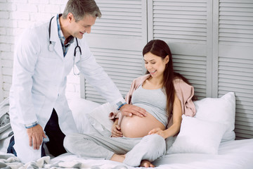 Everything is ok. Positive cheerful nice doctor smiling and putting his hand on a belly while...
