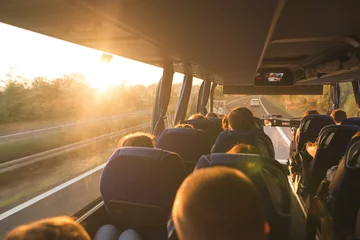 Foto op Plexiglas Background. Travel by bus. Bus interior. Salon of the bus with people fill the sun with light in the sunset. People travel on a big tourist bus. The bus rides along the mornings in the sunrise © bodnarphoto