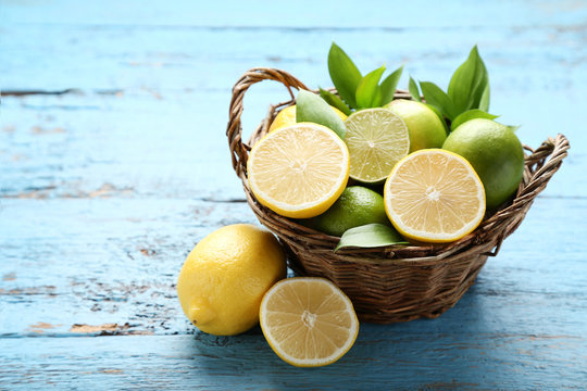 Lemons and limes with green leafs in basket on blue wooden table