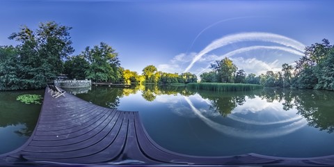 Early morning on a lake near a green forest in summer the sky with clouds. In the format of 360...