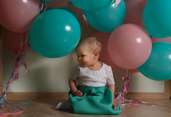 Fototapeta na wymiar little girl in blue and white dress next to balloons, smiling, holiday, year, birthday child. sits on the floor