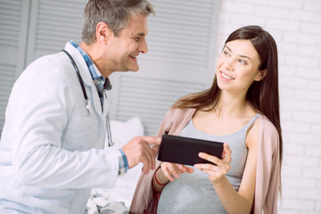 Modern technology. Delighted pleasant young woman holding a tablet and looking at her doctor while talking to him