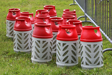 Composite gas cylinders of red and gray color in volume of 18,2 liters stand on a grass in city park for carrying out of colorful action with light and music