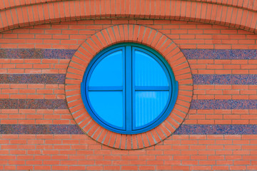 Red brick wall with round glassed window with reflection of blue sky