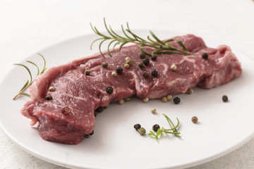 raw entrecote steak with rosemary and spices on a white plate