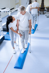 Development. Qualified reliable experienced medical worker touching the injured leg of her calm senior patient while being in a modern equipped rehabilitation center