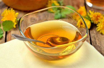 Close-up of dandelion jam in glass bowl, spoon, dandelion head around
