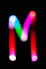 Letter M. Glowing letters on dark background. Abstract light painting at night. Creative artistic...