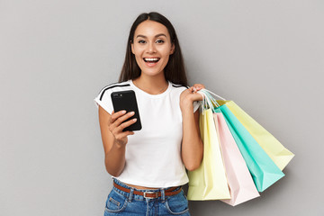 Cheerful woman holding shopping bags isolated over grey background using mobile phone.