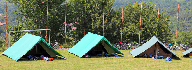 three green tents mounted by scouts in a meadow