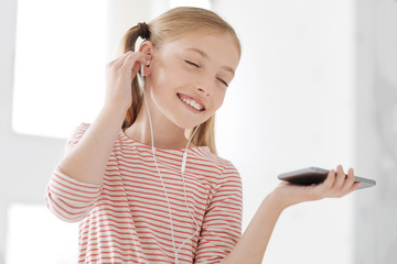 Music lover. Attractive girl keeping eyes closed and wearing earphones while being very pleased