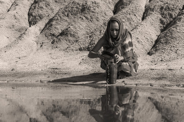 girl of oriental appearance in sari and hijab fills the pitcher with water from a dirty source in the arid area
