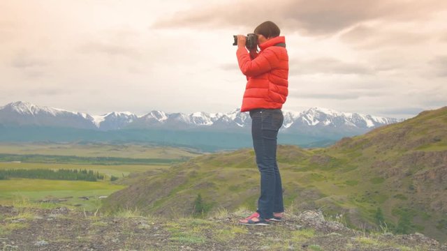 Woman photographer taking photo using DSLR camera outdoors on hike. Female hiker taking pictures outside living outdoor lifestyle in nature landscape. A woman in a red jacket, jeans with a camera.