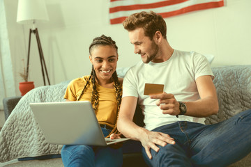 What should we buy. Smiling young people talking about their new flat while both sitting on the floor and doing online shopping at home.