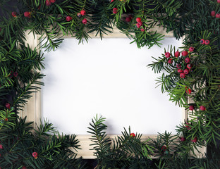 Creative layout made from Christmas tree branches with red berries and frame paper card note. Copy space for text. Nature New Year concept. Flat lay.