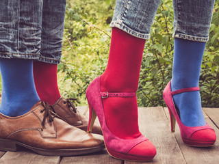 Legs of a young couple in stylish shoes, bright, colorful socks on a wooden terrace against the background of green trees. Lifestyle, fashion, fun