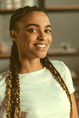 No time for worries. Waist up shot of a happy young lady with braids grinning broadly while looking into the camera indoors.