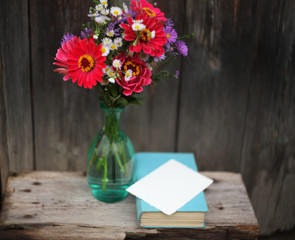 a summer bouquet with zinnias in a glass bottle ,and a book on the old wooden  bench/birthday /mother day/love card