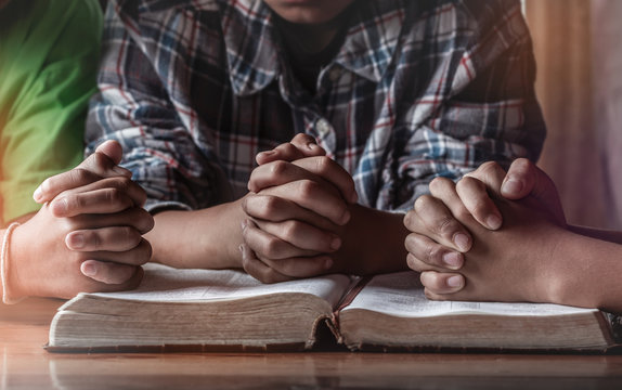 Children group praying on wooden table with open holy bible, prayer meeting concept