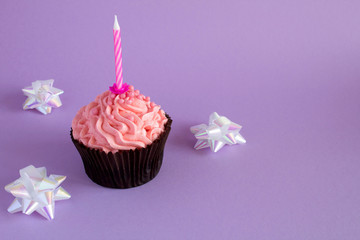 One cupcake with pink cream and candle on the violet background.Copy space.