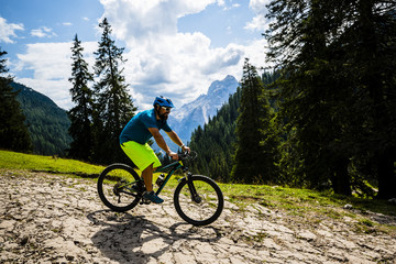 Fototapeta premium Tourist cycling in Cortina d'Ampezzo, stunning rocky mountains on the background. Man riding MTB enduro flow trail. South Tyrol province of Italy, Dolomites.