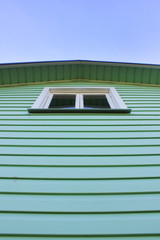 Rural Village House with Single Window and Striped Light Green Painted Walls on Empty Blue Sky Background. New Modern Rural House, Striped Wooden Wall with Single Window on Summer Day, Low Angle View