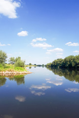 Fototapeta premium Clean water in the river. The water mirror reflects white clouds. A beautiful view on a sunny day.