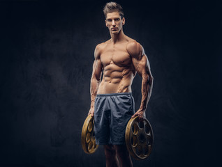 Fototapeta na wymiar Handsome shirtless ectomorph bodybuilder with stylish hair posing with a barbell disk on dark background.
