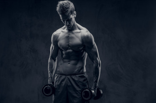 Black and white photo of ectomorph bodybuilder posing with dumbbells and looks down.