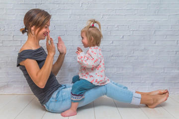 girl, the mother and child in front of a white brick wall playing Patty-cake and kiss